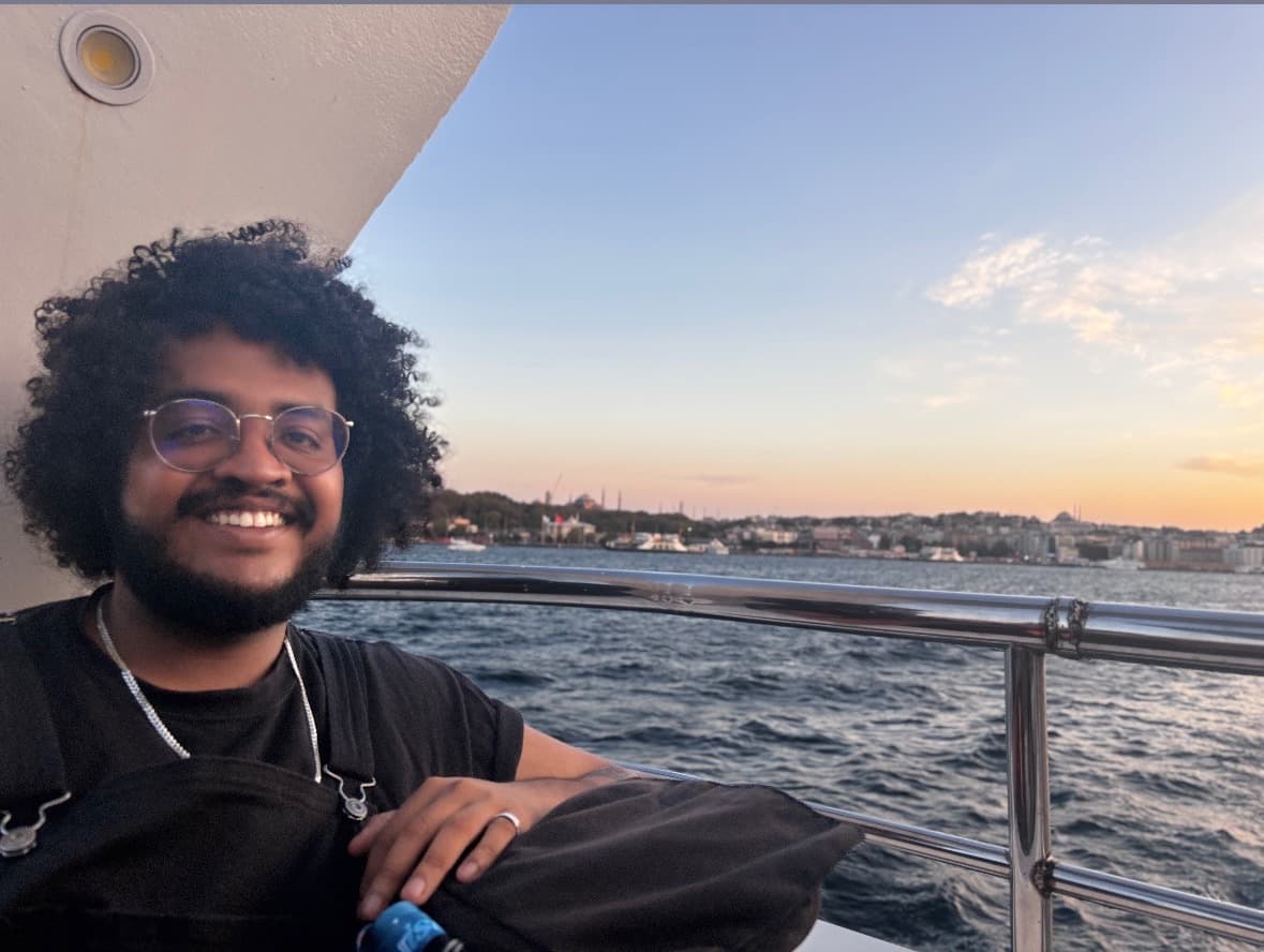 Alejandro smiling on a boat at golden hour, city skyline across the water behind him